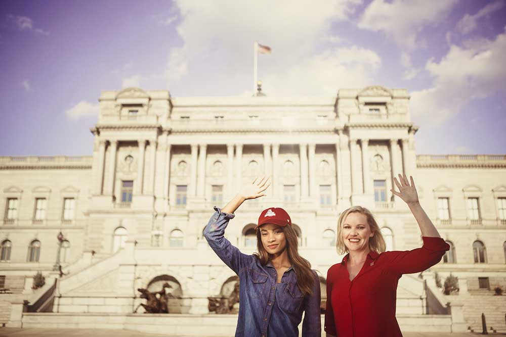 Two women in American university master's programs stand outside a building and wave.