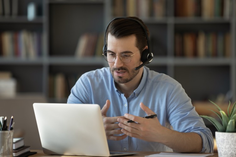 An online teacher using a laptop and wearing headphones leads a virtual class.