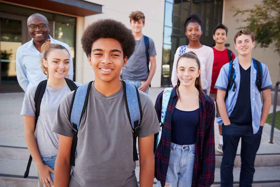 Diverse group of students pose in a group in front of their school building.