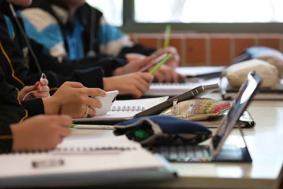 Children sit at a desk with their devices.