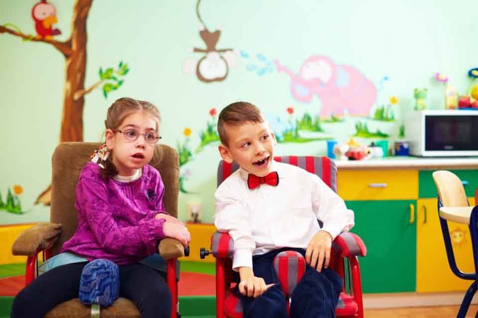 Two children with special needs sit in a classroom.