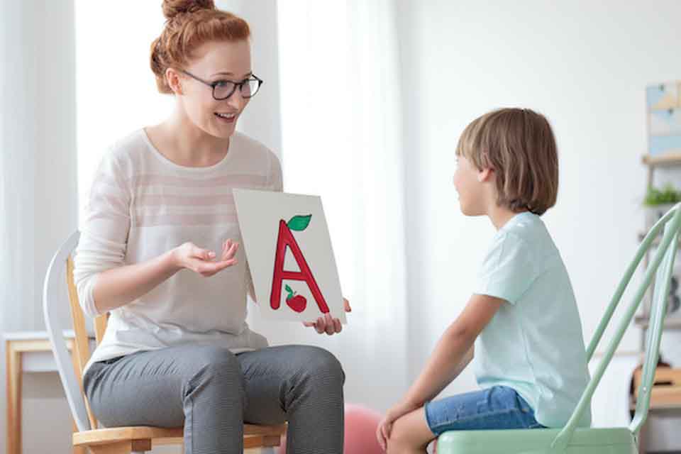 A female teacher holds up a card with an A in front of a young student