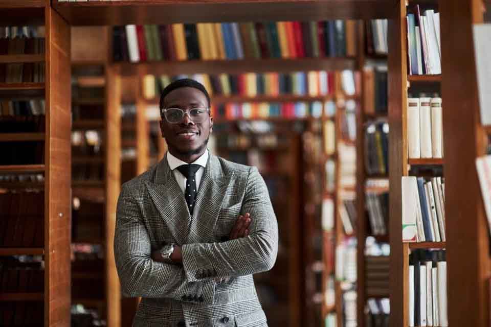 An EdD degree holder stands in front of a library bookshelf.