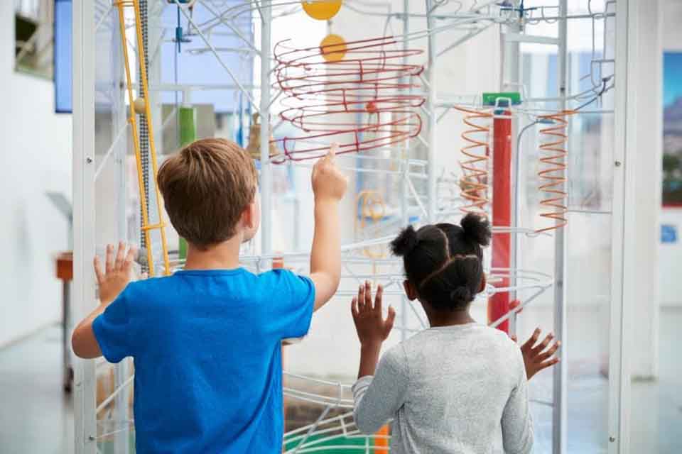 Two children seen from the back interact with a colorful science exhibit at a museum.