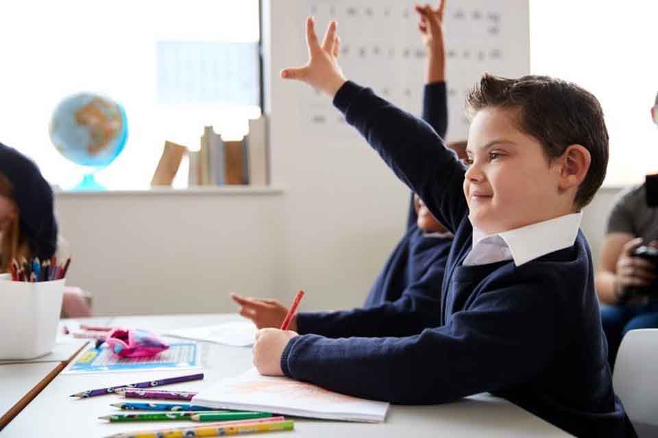 A student with Down syndrome raises his hand in class.