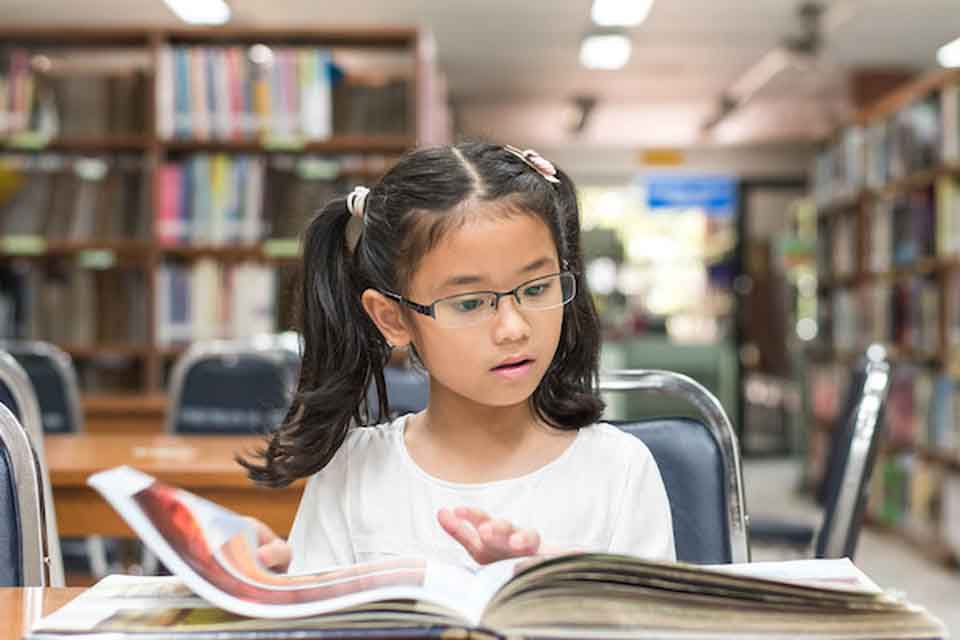 A girl looking at a book, she's seated in a library