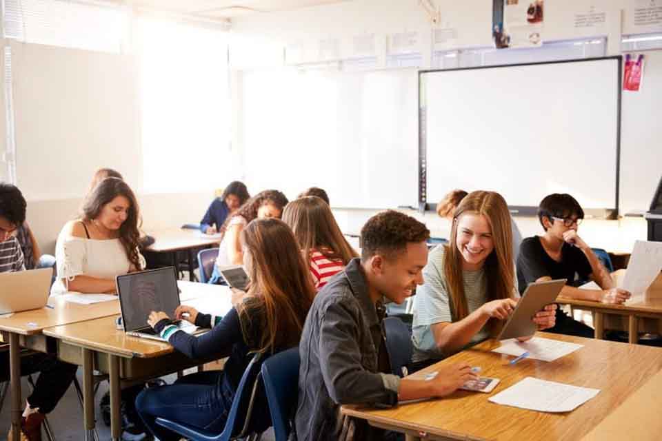 A group of students use their electronics while sitting at their desks.