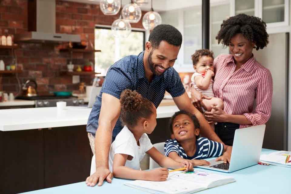 Smiling parents help their young children with homework at the kitchen table.