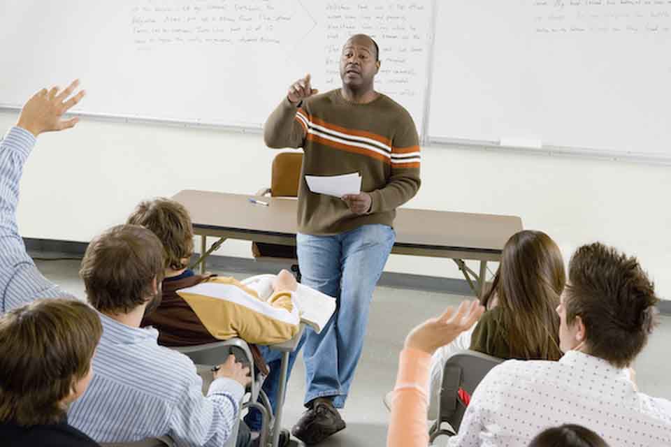 Postsecondary teacher asks classroom a question and picks on students to answer during his lecture.