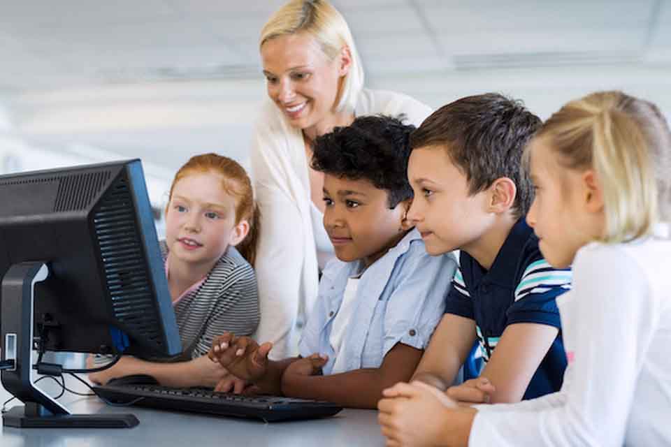 A female teacher shows her students something on a computer.