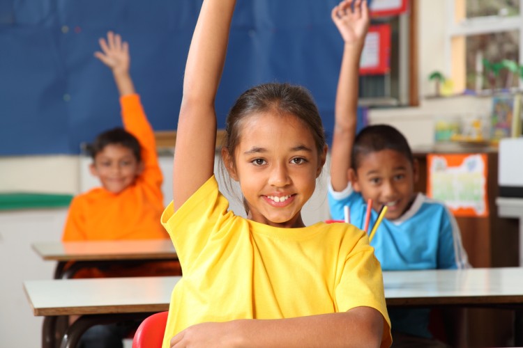 Students raise their hands in an elementary school classroom.
