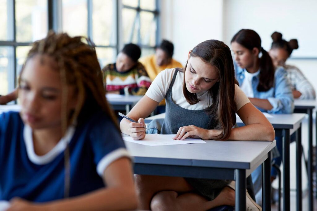 A group of diverse students in a classroom sit at their desks working on an assignment.