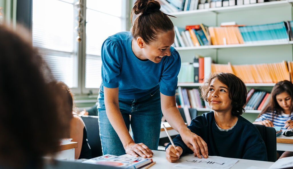 A teacher smiles as she helps a student with their school work.