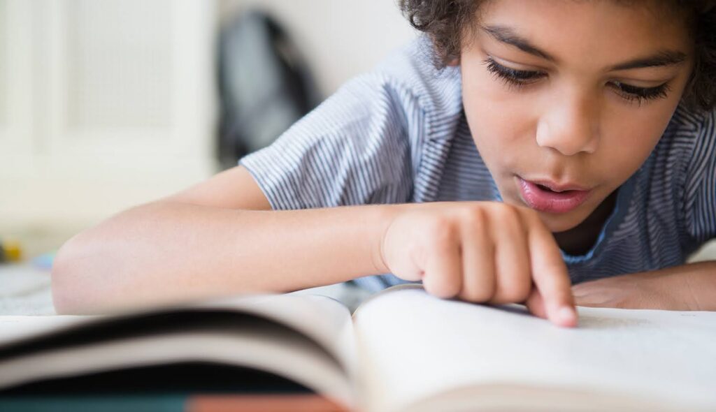 A young student traces his finger across the pages of a textbook as he reads.