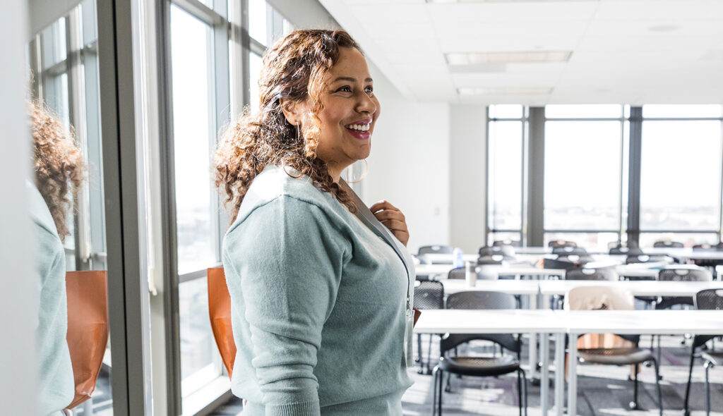 An educator smiles as she gazes out over an empty classroom.