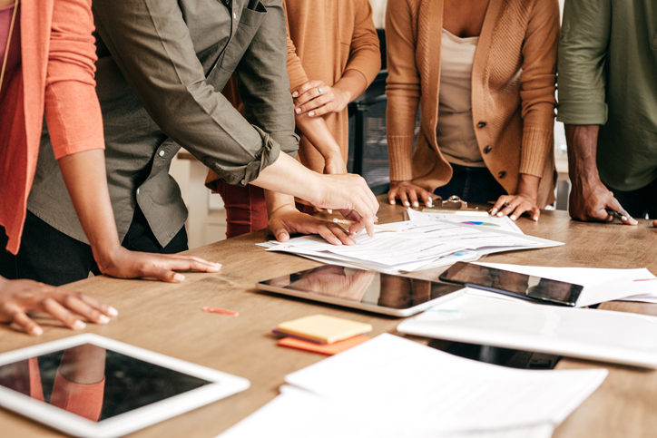 Education professionals work over a desk with documents and tablets.
