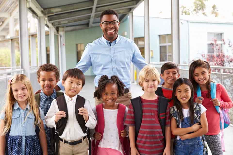 An elementary school teacher stands with a group of students.