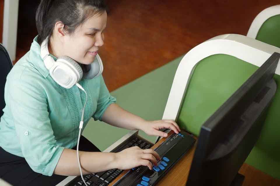 A high school student sits at a desk using a braille keyboard.