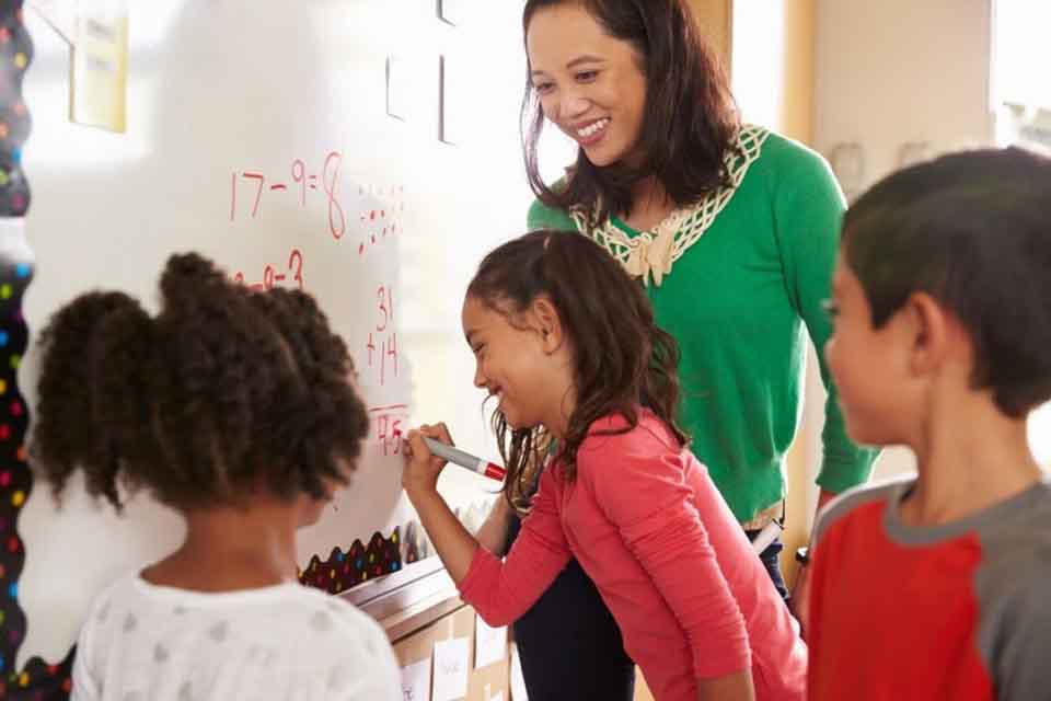 A teacher and students work on math problems on a whiteboard.