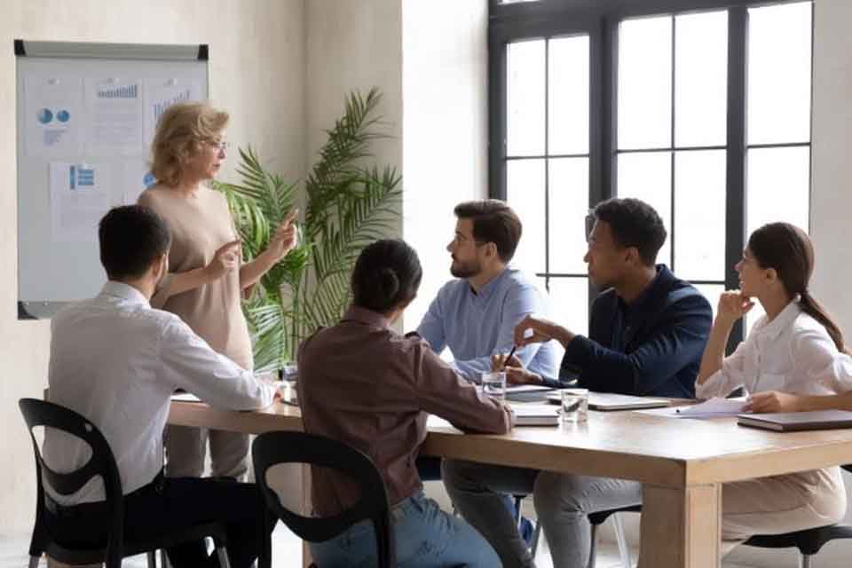 A chief learning officer stands at a table speaking to a group of people.