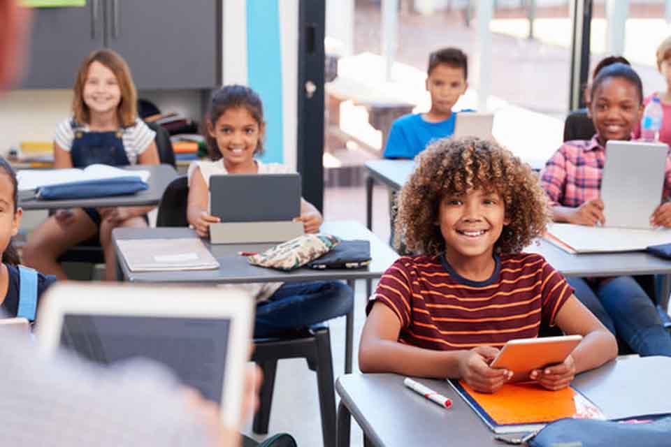 A classroom with children seated and smiling at the teacher