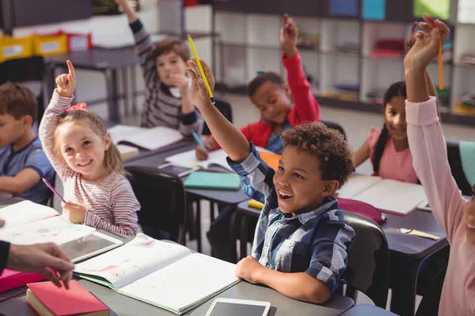 Children in a classroom, some have their hands raised