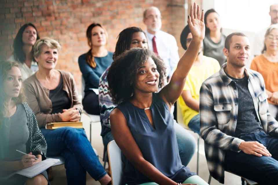 A smiling person raises their hand during an education program in a workplace.
