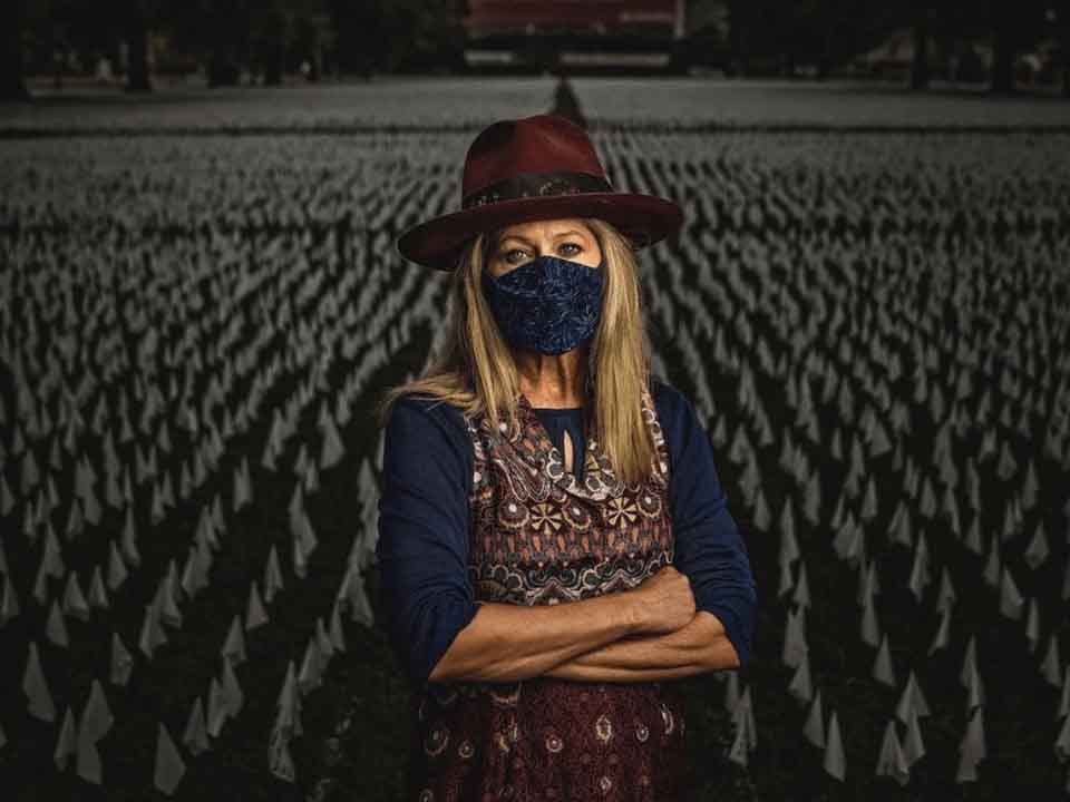 Artist Suzanne Brennan stands in front of white flags commemorating lives lost to COVID-19.