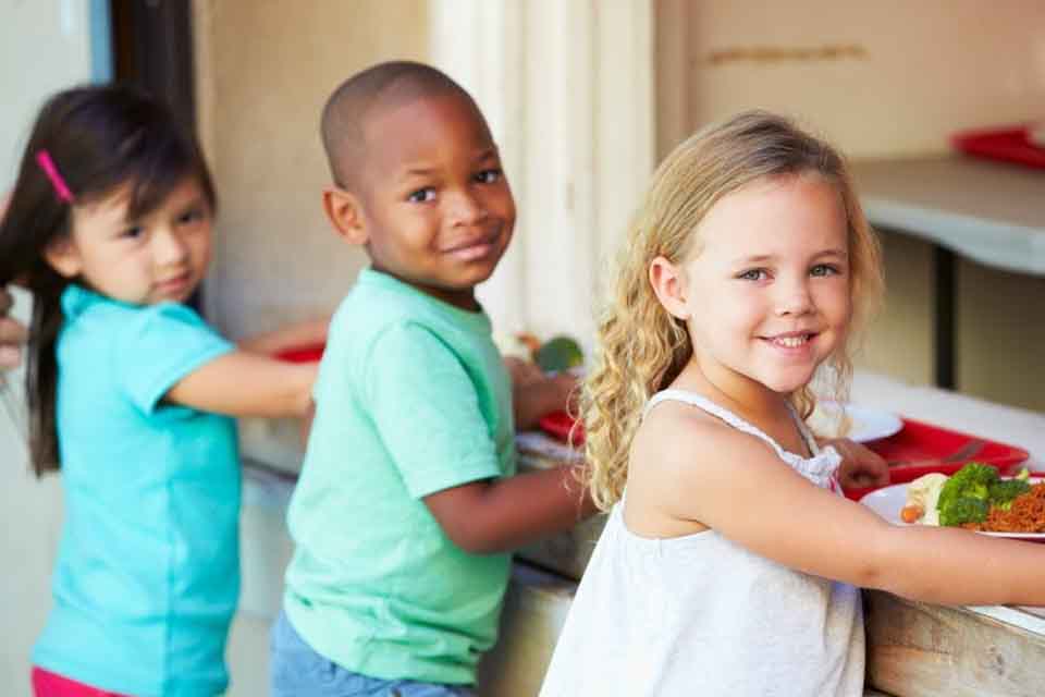 Children sit at a table eating their lunches.