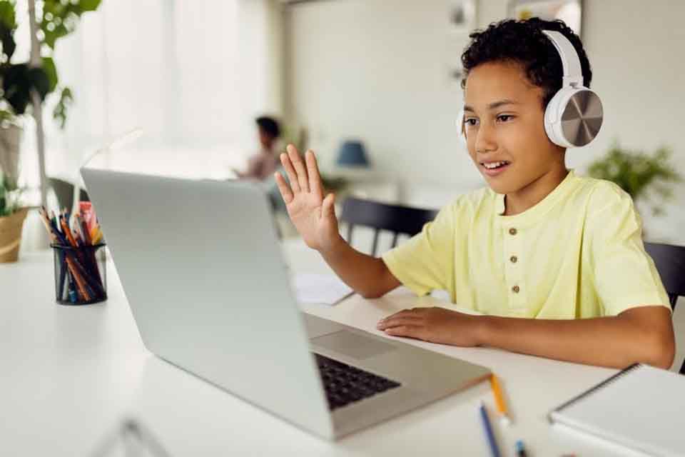 An online student waves to their teacher through their laptop