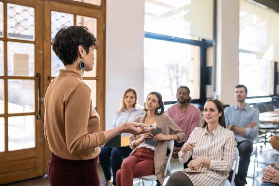 A school administrator presents to a group of teachers sitting in chairs.