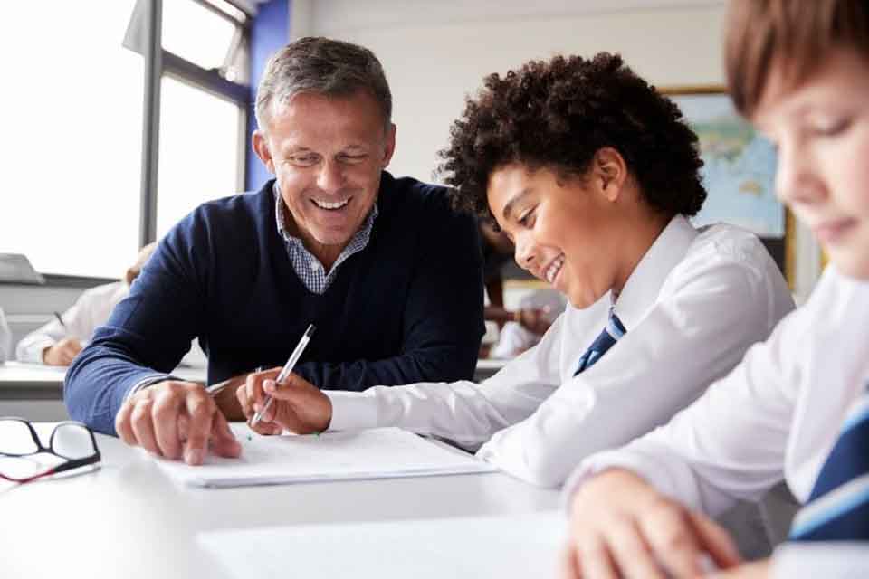 A teacher helps a smiling student with an assignment.