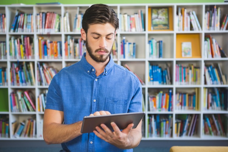 A curriculum developer stands in a library working on a tablet computer.