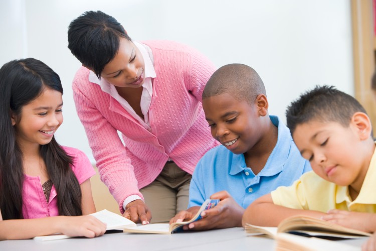 A learning specialist helps three elementary school students in a reading group.