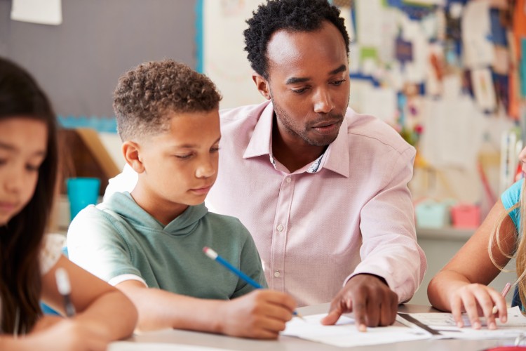A teacher works with a student at a desk.