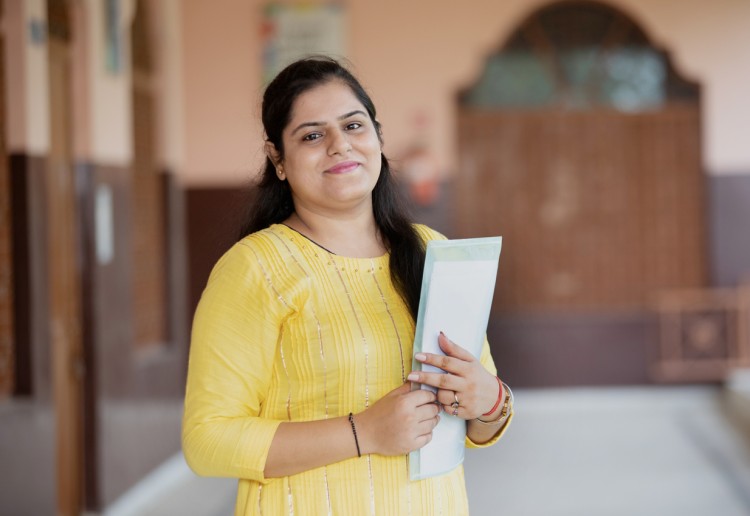 A school principal holding a folder stands in a hallway.