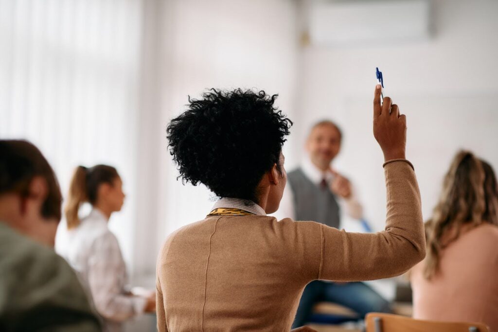 A student in a lecture hall raises her hand to answer a question.