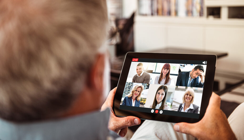 A man participates in a teleconference with six other adults.