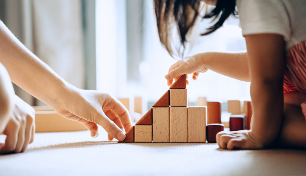 A closeup of a teacher and a child's hands using wooden blocks to build a tower.